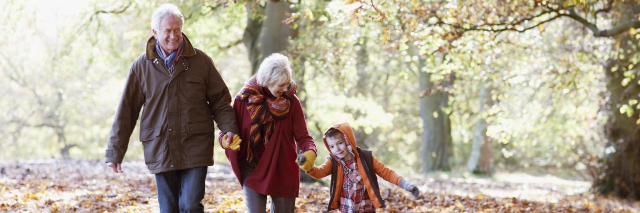 two grandparents hand in hand with their grandson walking in a park