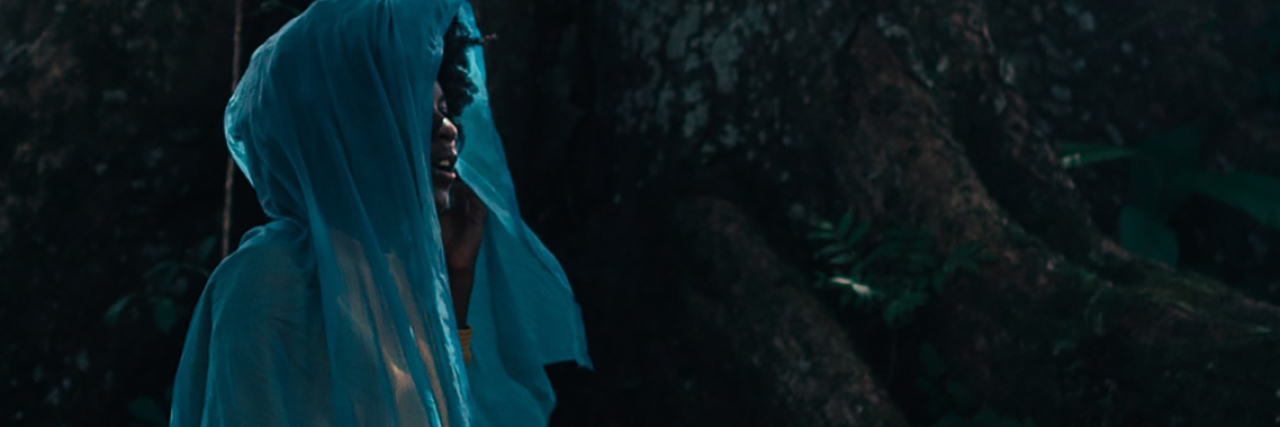 A Metaphor for Depression When It Feels Like It Won't Go Away photo of woman, the contributor, sitting on tree stup with blue scarf around face and head