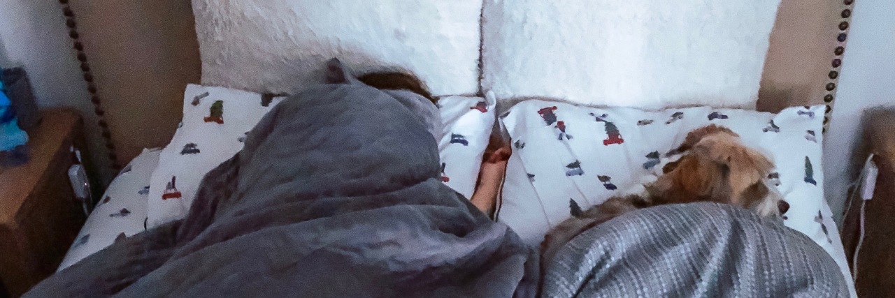 Going Back to Work After the Holidays With Chronic Migraine woman lying in bed with her dog