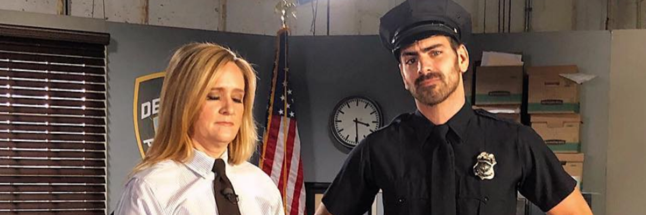 Samantha Bee in a white shirt and tie with Nyle DiMarco in a police uniform.