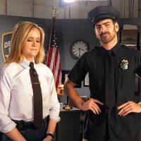 Samantha Bee in a white shirt and tie with Nyle DiMarco in a police uniform.
