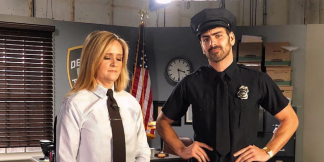 Samantha Bee in a white shirt and tie with Nyle DiMarco in a police uniform.