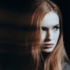 Woman with red hair looking suspiciously over her should. There's a blurred image of her face next to her.