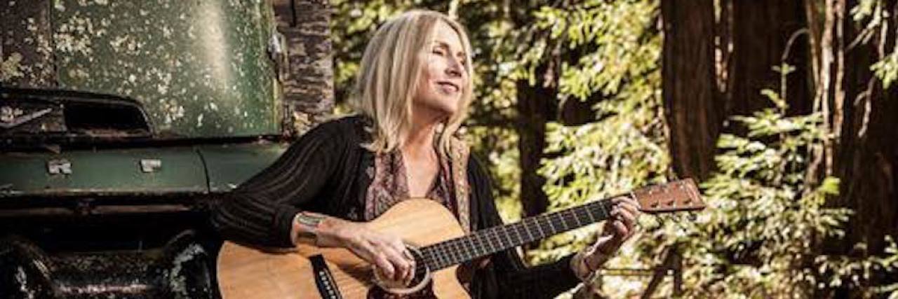 Pegi Young with guitar and a black dog nearby
