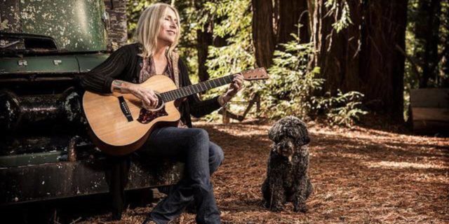 Pegi Young with guitar and a black dog nearby