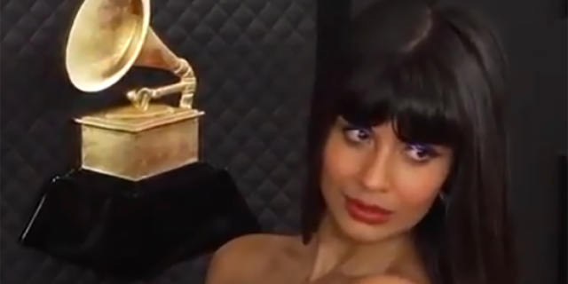 Jameela Jamil is wearing a purple dress and looks at something offscreen on the red carpet