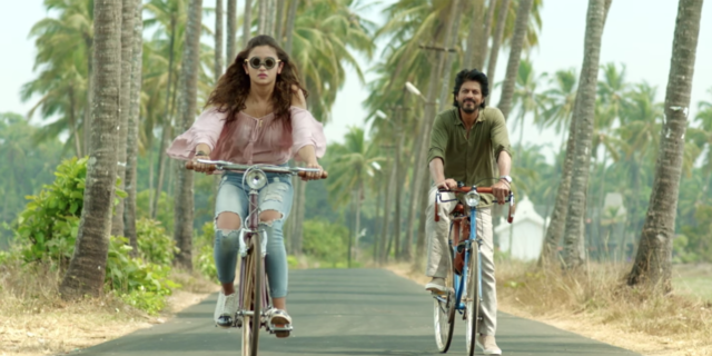 still image of bollywood movie Dear Zindagi showing male and female actors riding down tree-lined road on bicycles