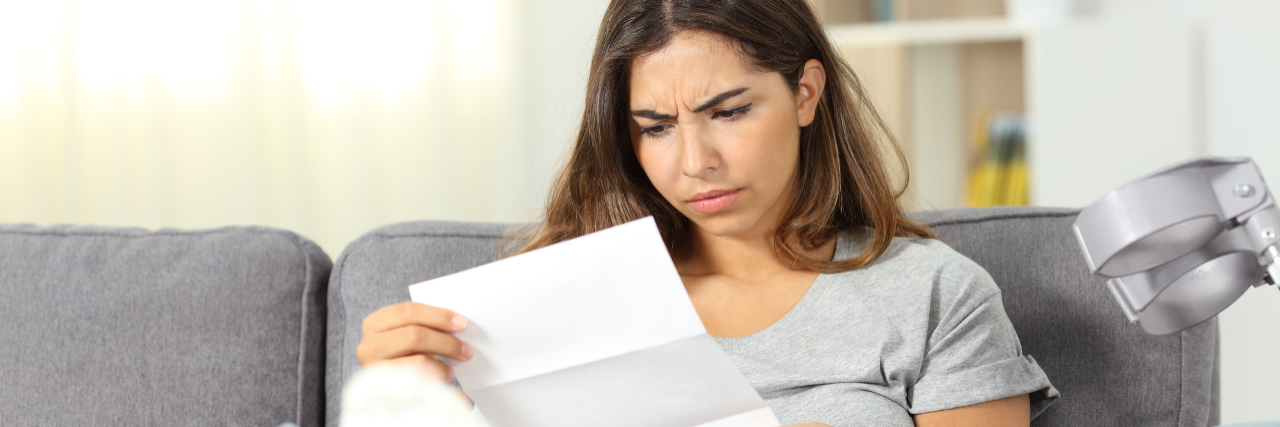 What Are Short-Term Health Insurance Plans? Woman sitting on a couch with a broken leg looking worryingly at a letter.