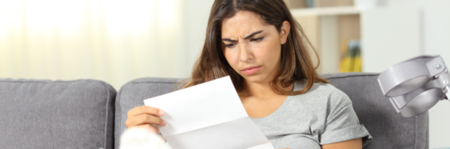 Woman sitting on a couch with a broken leg looking worryingly at a letter.