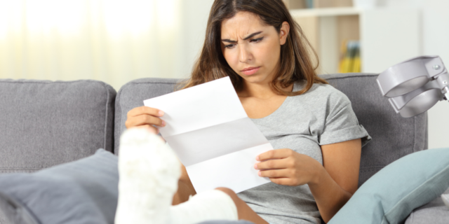 Woman sitting on a couch with a broken leg looking worryingly at a letter.