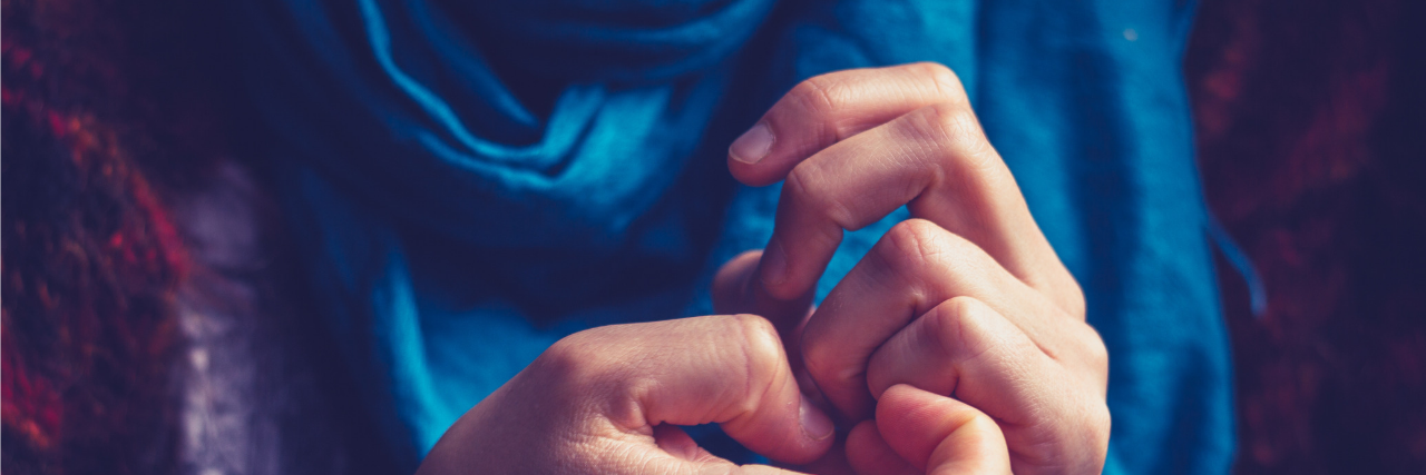 Habits and Symptoms of Bipolar Disorder Close up of woman wearing blue scarf and picking at her nails.