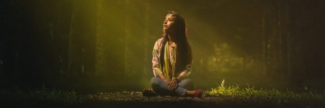 young woman sitting in forest in middle of green light