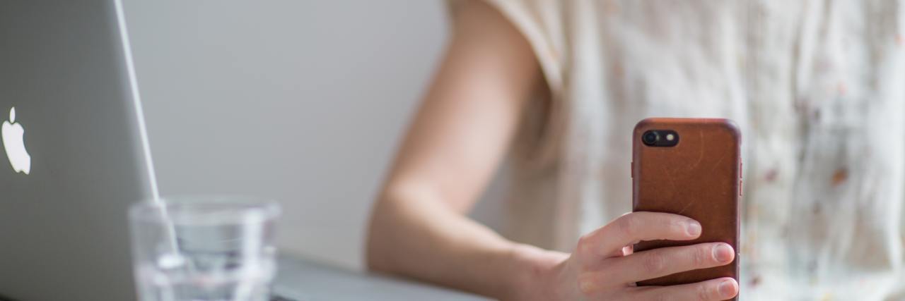 How FOMO Keeps Me Going in Life With Chronic Illness woman sitting in front of computer looking at phone