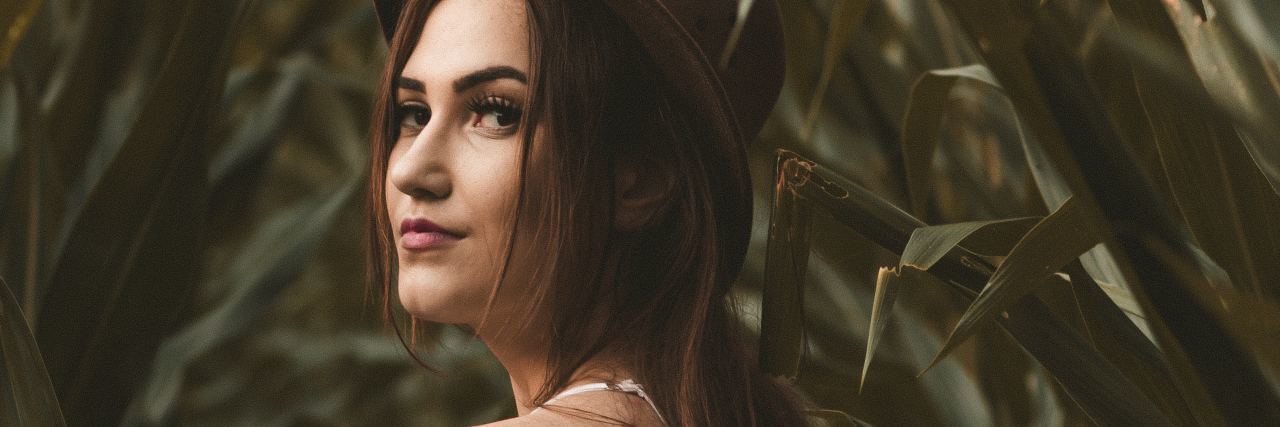 You Shouldn't Be Ashamed for Working Less for Your Mental Health photo of woman in white dress and brown hat standing among long leaves and smiling