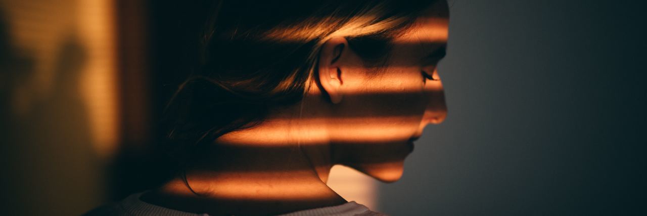 Anxiety: I Find It Hard to Forgive People woman in profile with eyes closed and serious expression, while stipped sunset light and shadow falls on her from window