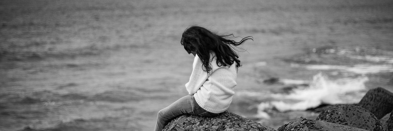 Finding Out Why Sex Was Painful With My Ex-Partner black and white photo of woman sitting on rocks by ocean under stormy sky