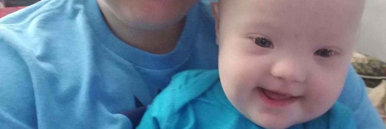 Finding Direction After a Down Syndrome Diagnosis Mother holding baby with Down syndrome. They are both wearing pastel-blue shirts.