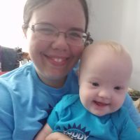 Mother holding baby with Down syndrome. They are both wearing pastel-blue shirts.