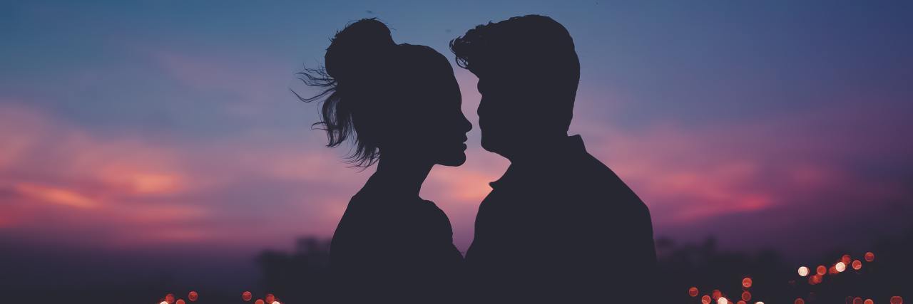 silhouetted man and woman standing close together at sunset