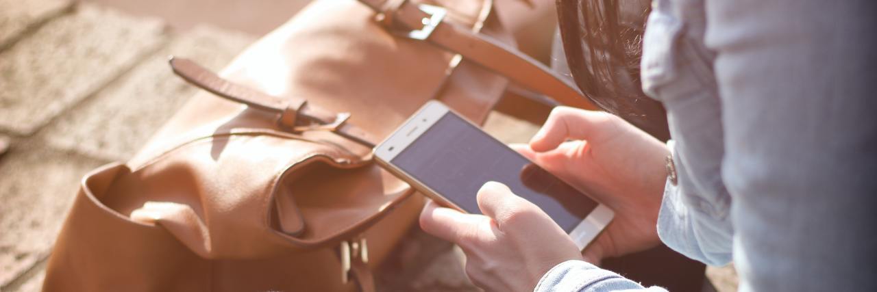 Why I Changed the Way I Use Social Media With Chronic Illness woman sitting on ground looking at smartphone