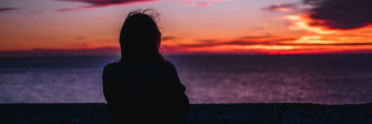 photo of silhouetted woman standing looking at sunset