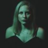 photo of blonde woman standing in darkness looking at camera with serious expression