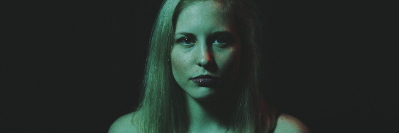 It's Not Ok That Millennials Are Struggling With Mental Illness photo of blonde woman standing in darkness looking at camera with serious expression
