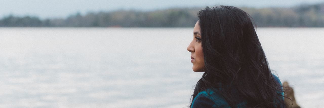 Why Embracing Brené Brown's Vulnerability Is Hard With Mental Illness side profile of a woman with long dark hair standing by a lake on a cloudy day