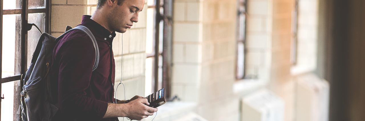 How I Struggle and Feel Abandoned Waiting for a Text With BPD photo of young man leaning on wall in hallway looking at his phone