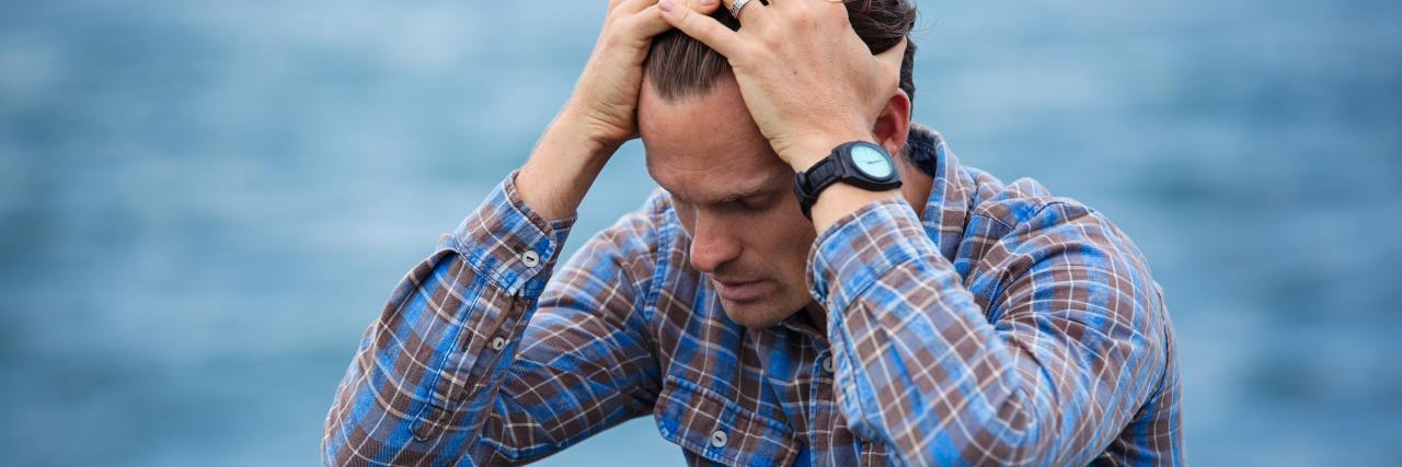 How the Navy’s Treatment of My Problems Led to My Suicide Attempts photo of man depressed sitting by ocean with hands on forehead