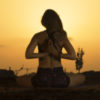 photograph of woman in yoga pose against sunset with hands behind her back in prayer pose