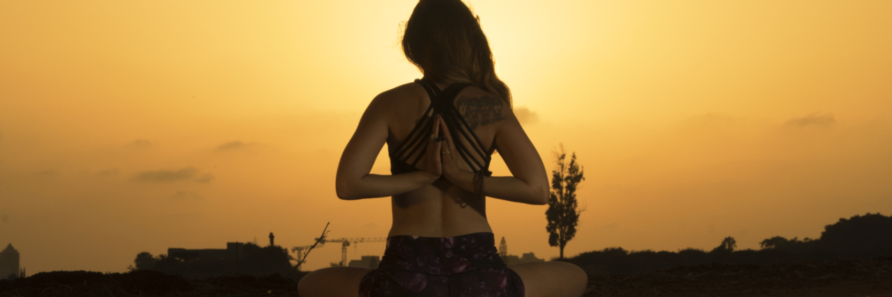 photograph of woman in yoga pose against sunset with hands behind her back in prayer pose