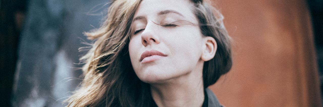 What People Should Know About Life With Chronic Illness woman with long brown hair standing outside with her eyes closed