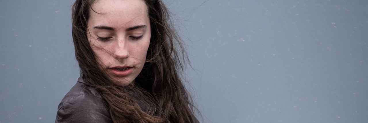 close up portrait photo of woman looking down worried against gray background