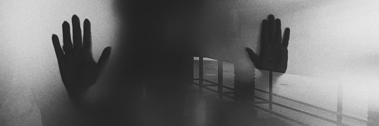 Mental Health Care Must Keep Changing Its Cruel Origins black and white spooky photo of someone's hands pressed against glass