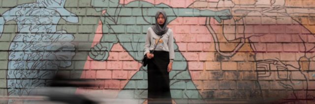 photo of young indonesian woman standing against wall with soccer mural wearing hijab and looking into camera