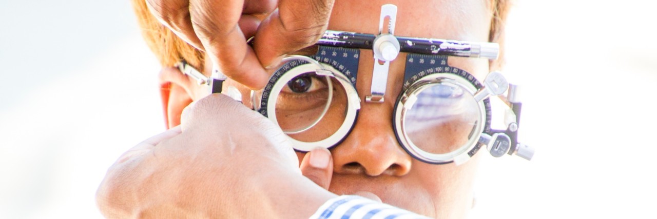 Why Eye Exams Are Important A man in a blue sweater is getting testing glasses placed on his face by an optician in a white coat