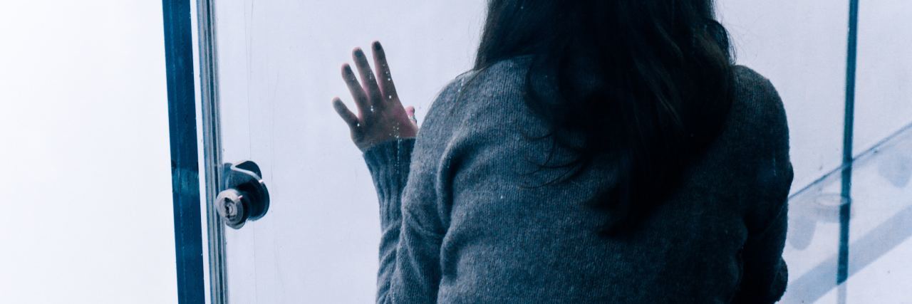 Depression Feels Like Being Isolated Inside a Glass Box photograph of woman alone in glass sky box with hand against glass