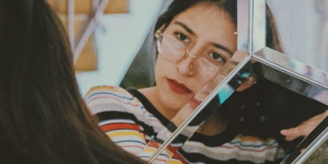 photo of dark-haired woman looking into mirror with concerned look