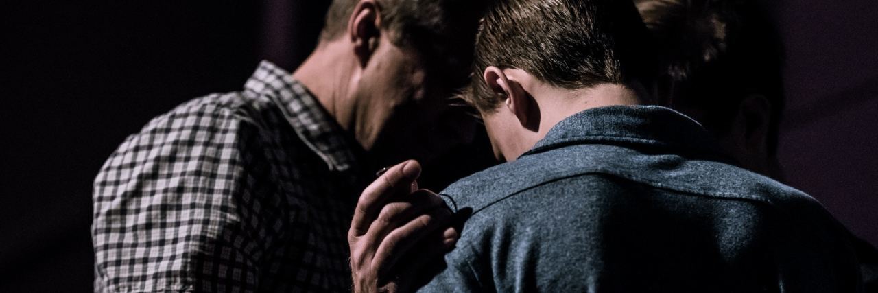 How to Help Someone You Love With Bipolar Depression two men in semi darkness with one man's hand on the other's shoulder in support or prayer