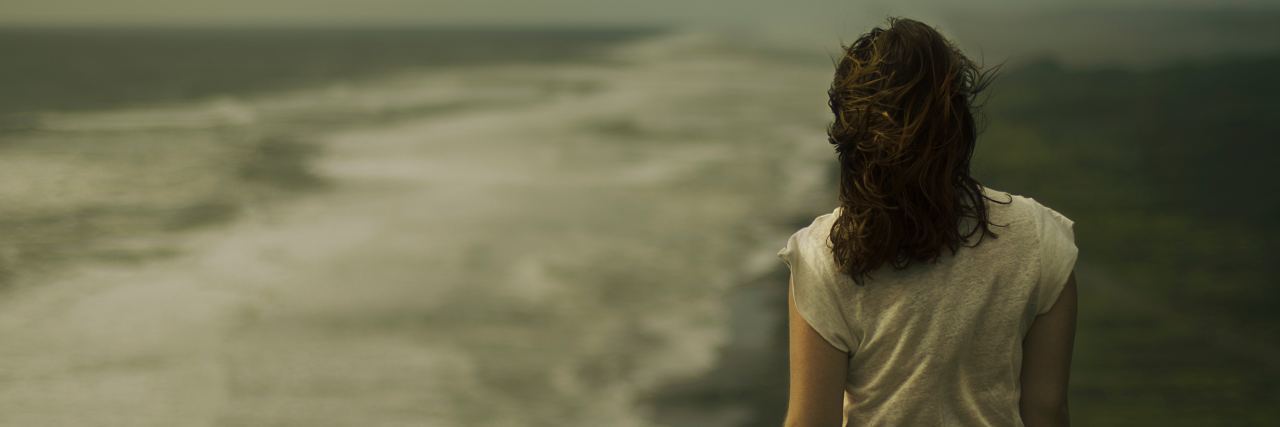 dark photo of woman standing on beach looking at horizon