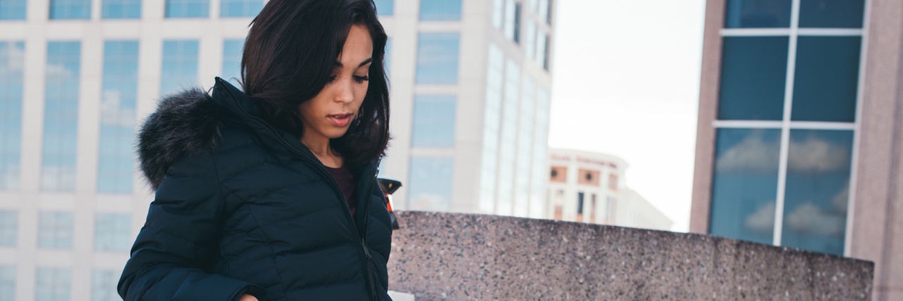 What It's Really Like to Be an Outgoing Person With Social Anxiety woman looking down while leaning on a wall