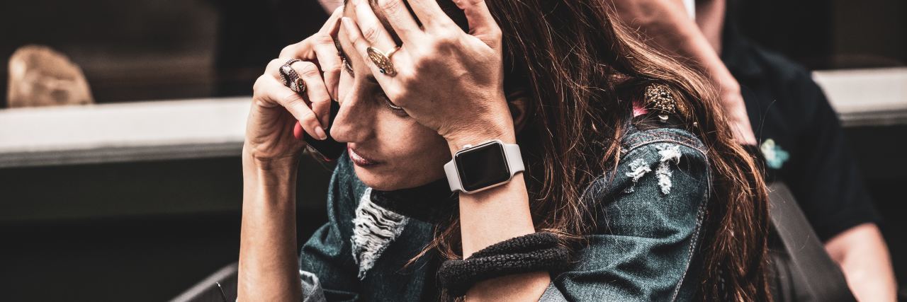 How to Cope With Anxiety and Small Changes in Plans photo of woman on phone sitting down and looking stressed with her hand raised to her forehead