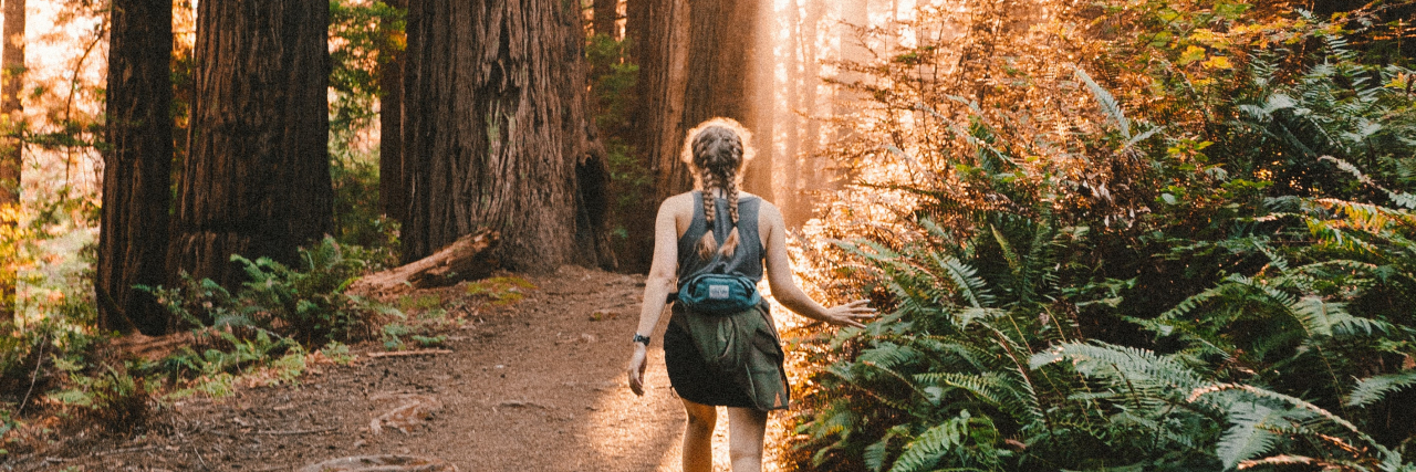photo of a woman hiking through sunny forest