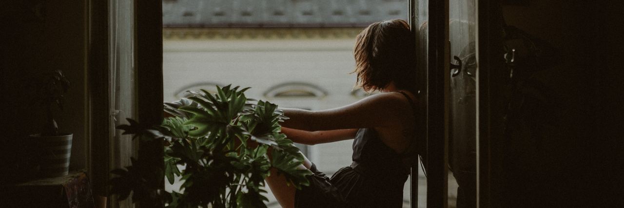 dark photo of woman sitting on window sill looking out over rooftops