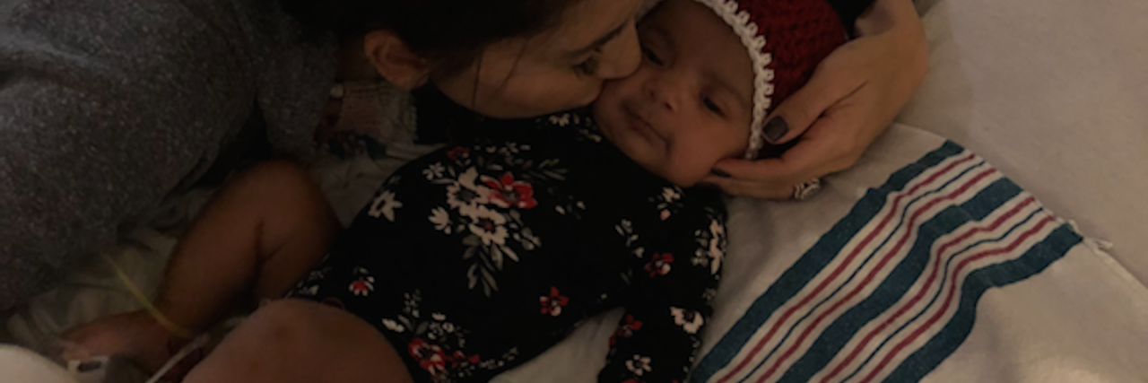 A mom leans in to kiss her baby that is in a hospital bed.
