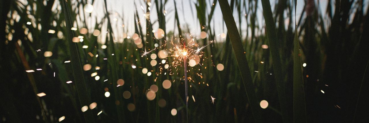 close up point of view photo of person holding sparkler in field at dusk