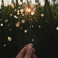 close up point of view photo of person holding sparkler in field at dusk