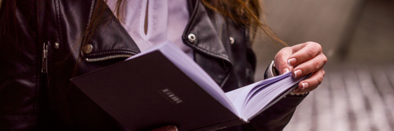 photo of woman wearing leather jacket and reading from book or journal