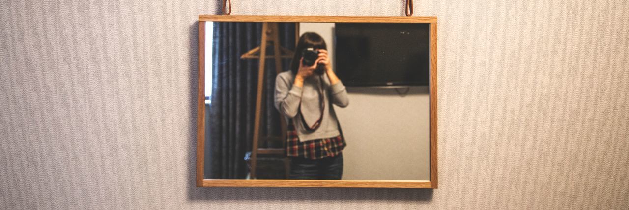 Losing and Reclaiming Control in Eating Disorder Recovery selfie taken by woman photographing herself in mirror below shelf with books and bottles